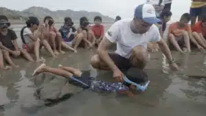 Sebastián Hernández supports a child practicing in shallow water while other children watch on the beach in Ligüiqui, Ecuador.