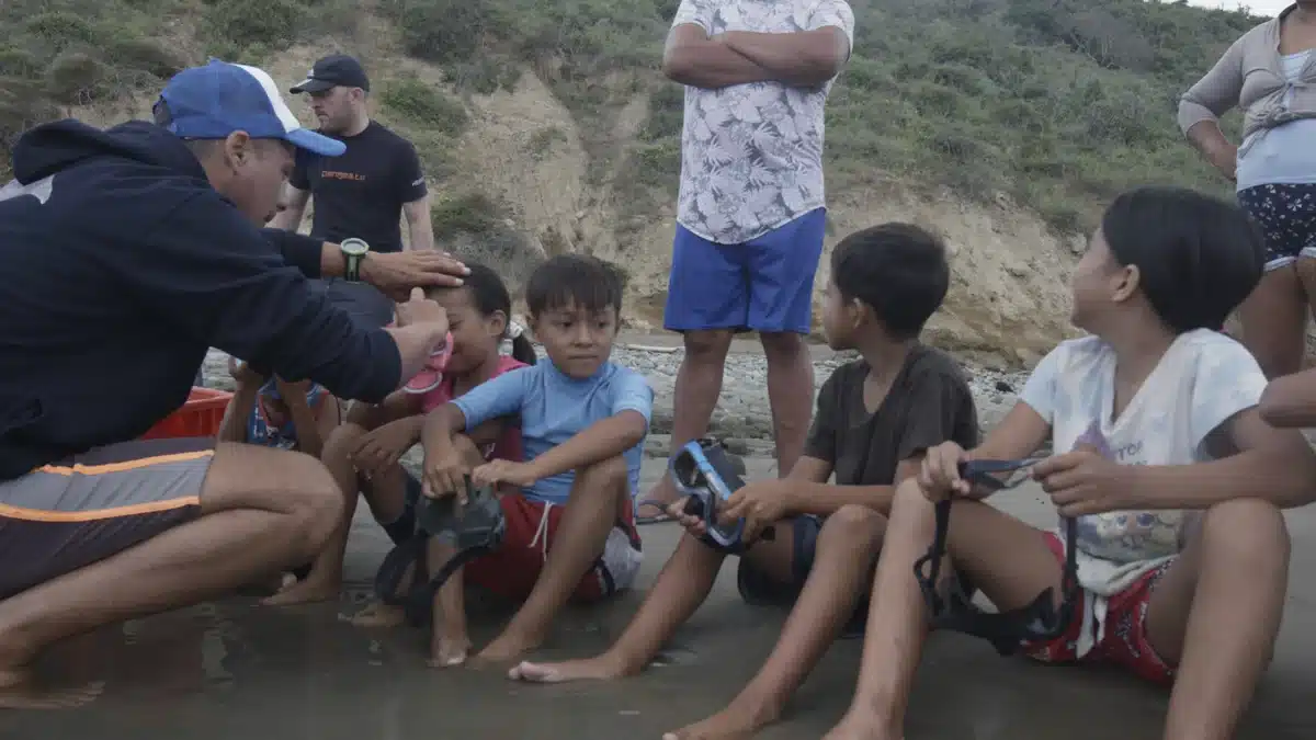 Sebastián Hernández shows masks and water equipment to children seated at the shoreline in Ligüiqui, Ecuador.
